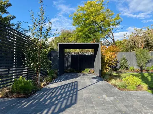 Between fence and lawn with planted beds, Black granite plank paving runs lengthways to garden shelter. Built by Natural Spaces.