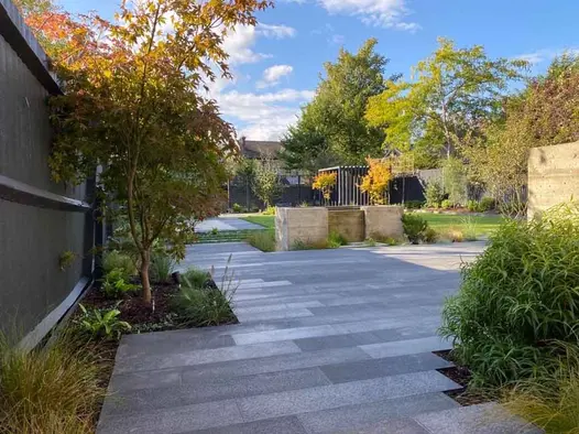 Expanse of Black Granite plank paving with narrow planted border next to fence and rectangular cut-in with shrubs.