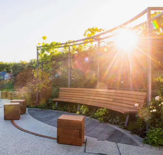 Tall hedge behind curved bench cantilevered above almond-shaped insert of Black Granite plank paving set into resin-bonded gravel.