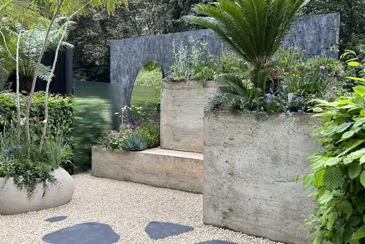 Large concrete block create statement piece surrounded by pebbles and planting, black slate cladding used in vertical lines on feature wall.