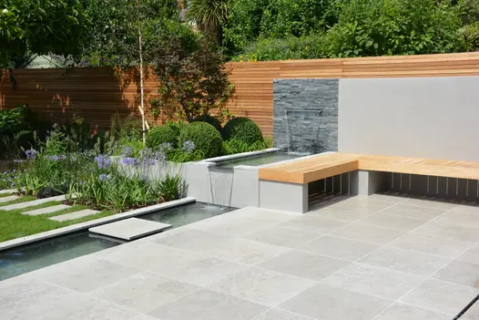 Waterfall feature using black slate cladding and porcelain, water falls 2 levels into pond that seperates lawn and patio.