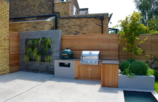 Living wall is clad with black slate cladding against wooden fence which leads to bbq area and pond water feature.