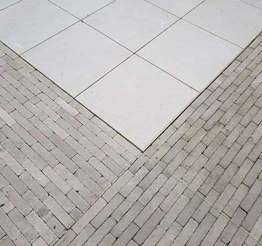 2 wide bands of Stone Grey clay pavers, laid at right angles to each other form edge of paved area of square slabs.