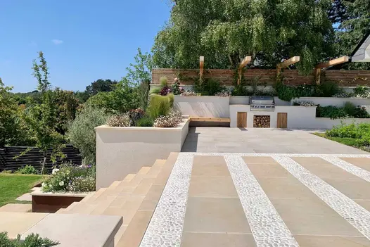 Multi level garden with outdoor cooking area and patio, steps lead down to lawn with raised flowerbeds using harvest coping stones.