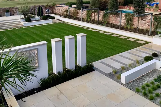Large square lawn with Harvest sawn sandstone slabs spaced as stepping stone along 2 sides and matching patio areas at either end.