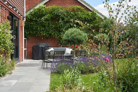 Narrow patio runs along back of house with clay paver strip leading from double doors, outdoor furniture, lawn and shrubs