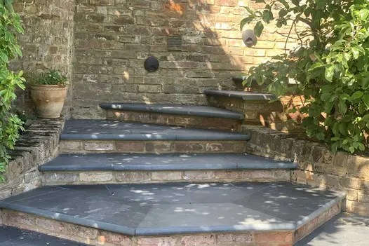 Brazilian black slate steps with bullnose edge rise from 3-sided platform and turn to ascend between brick wall and planted bed.