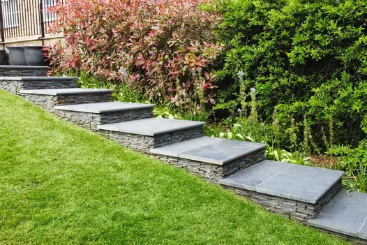 8 square steps each comprising Brazilian black slate bullnose  step tread and matching slab rise up sloped lawn by hedge.