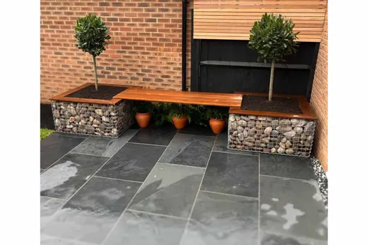 3 planted pots evenly spaced under planter bench of wood and gabions on Brazilian black slate patio. Design by Utopia Landscapes.
