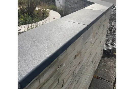 View along stone-clad wall capped with Brazilian Black slate coping to corner where an empty shopping trolley stands.