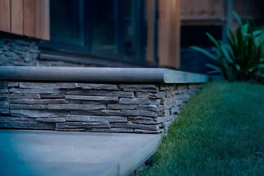 Eye-level view of Brazilian Black Slate bullnose step tread on stacked slate riser, next to grass slope.