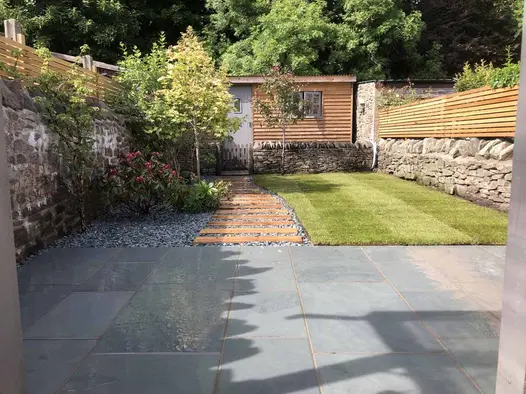 Wide plank path leads between lawn and gravel-mulched bed from Brazilian grey slate patio to wood-clad office.