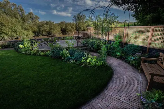 Path of Abbey Dark Multi clay paving curves between lawn and planted border to patio, passing under rose arches.