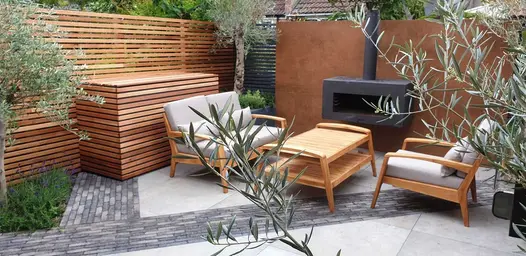 Outdoor lounge set and black stove on grey paving with stripes of Silver Grey Multi Clay Pavers. Design by Greenbird Gardening.
