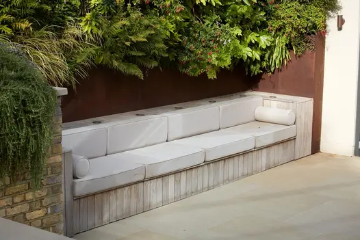 Deep-cushioned settee built against wall under foliage, with Britannia Buff sawn York stone paving at its feet.