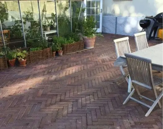 Dappled area, with wooden dining set and greenhouse against white wall, paved with Bromley clay paving bricks laid herringbone.