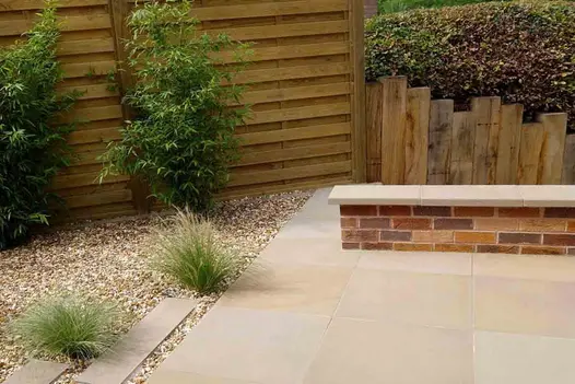 Fenced triangular gravel area adjacent to paving with low brick wall topped with Buff smooth sandstone pencil round coping.
