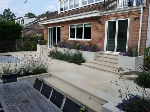 Multiple harvest sawn sandstone products including coping stones seen against red brick house with purple plants.