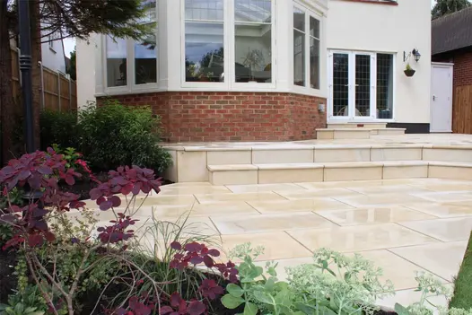 Harvest smooth sandstone bullnose steps rise to patio outside folding doors and deep bay window. Built by Essex Garden Designs.