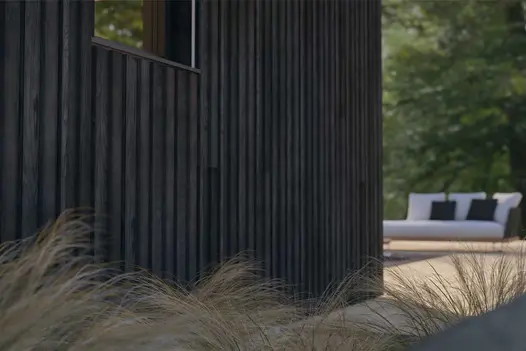 Exterior wall clad with Burnt Cedar Millboard Board and Batten cladding, used on a contemporary garden building with soft landscaping and garden furniture.