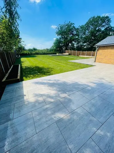 View across a large back garden on a summers day.  Patio paved in Travertine Dark Porcelain with dark grout.