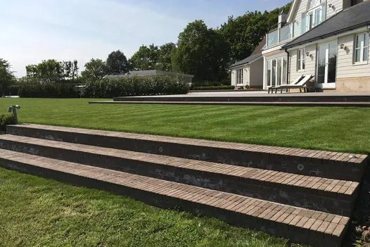 Three long steps clad with Aldridge clay pavers, set against a large lawn, trees, and a house in the background.