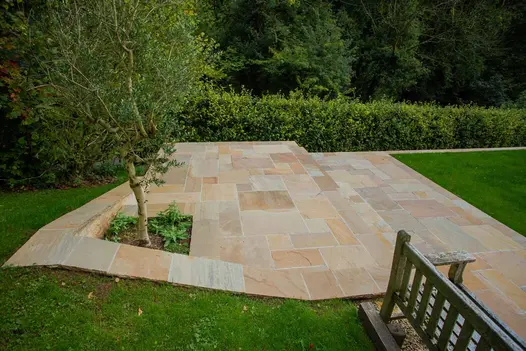 Lawn above and below 2-level Camel Dust sandstone garden patio that rises at one corner to create planting pit for small tree. 