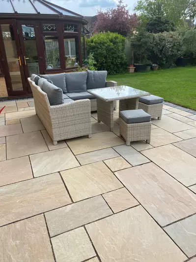 Conservatory at far end of patio of Camel Dust Indian Sandstone project pack paving next to lawn with shrub border.