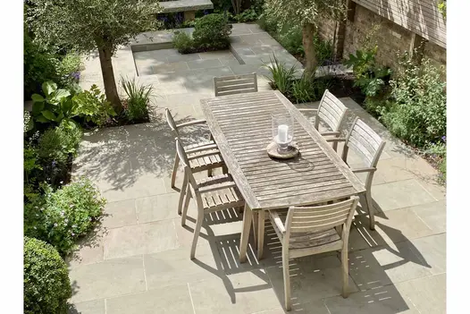 Narrow town garden paved with Heath smooth sandstone paving on different levels. Wooden dining set in foreground. 