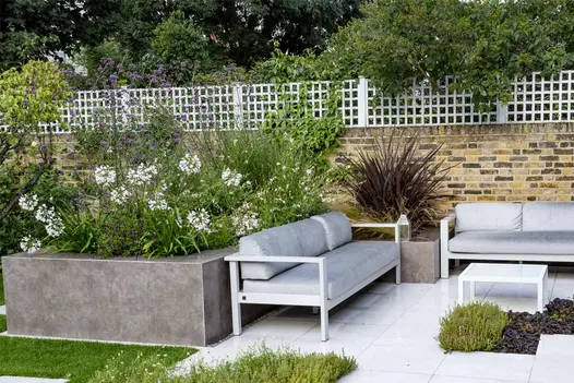 Raised flowerbeds clad in Vulcano Ceniza designclad are filled with wildflowers and positioned beside an outdoor sofa.
