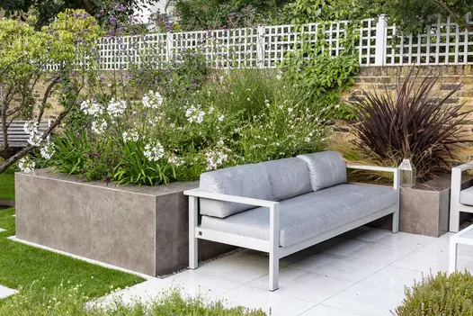 Raised flowerbeds clad with vulcano ceniza designclad filled with wild flowers, next to outdoor sofa.