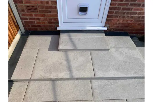 2 shallow steps down from back door to light grey patio edged with Charcoal porcelain planks. Built by C and C Agricultural.