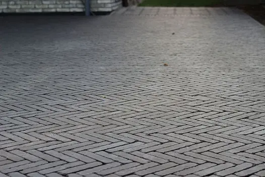 Low shot of charcoal grey clay pavers laid in a herringbone style, sunlight setting in the background.