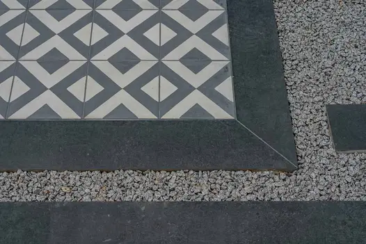 A close-up view of Charcoal Porcelain Planks arranged in a staggered pattern, forming stepping stones with pebbles interspersed.