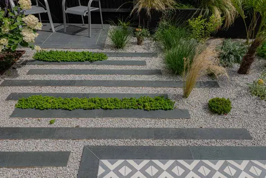 Staggered arrangement of Charcoal Porcelain Planks forming a pathway to seating area, with pebbles interspersed.