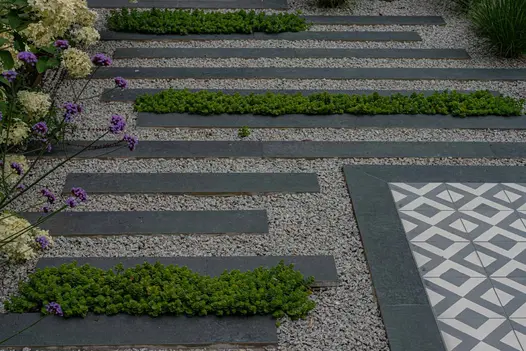 Patio pathway made of staggered Charcoal Porcelain Planks leading to a seating area, with pebbles nestled in between.