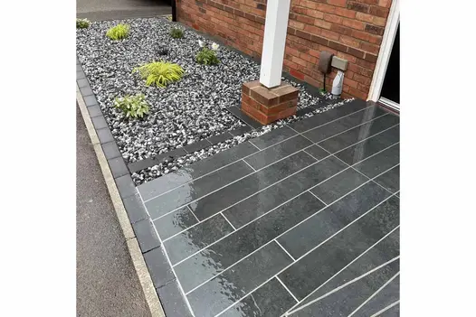 Close-up image of Charcoal Porcelain Planks laid next to area featuring gravel and a few plants, pointed with white grout.