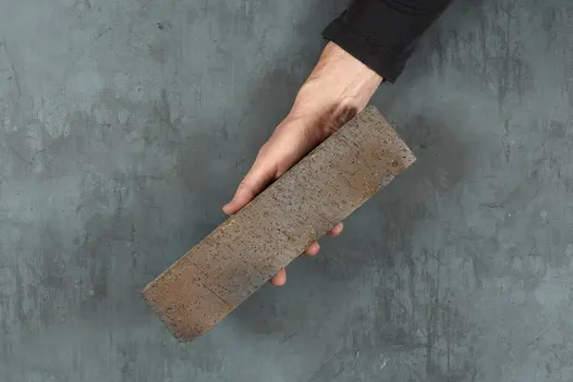 Against grey background, a hand holds Chelsea clay paver at angle. Available across the UK with free next-day delivery.