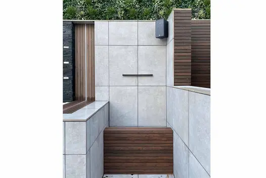 Modern water feature made out of porcelain paving, featuring Chestnut Composite Screening Battens and outdoor speaker.