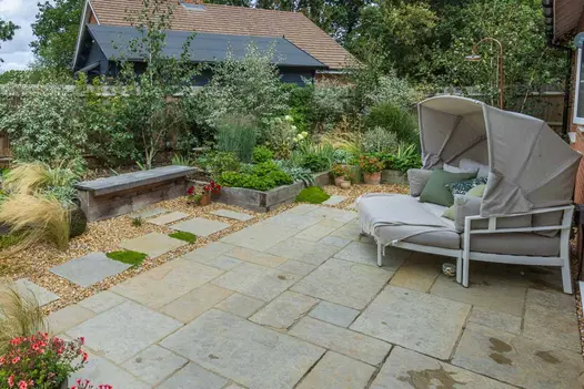 Day bed with canopy on square patio of Antique Yellow limestone paving, edged with gravel, timber sleeper bed and bench.
