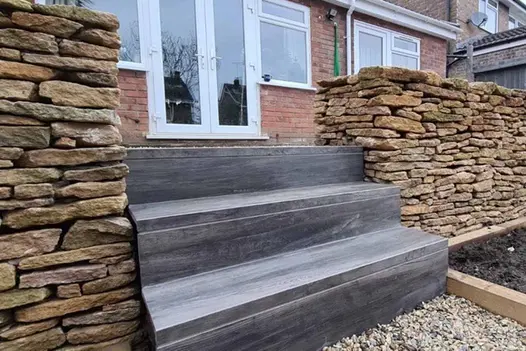 Cinder Porcelain 40mm downstand steps that have dark wood-effect finish between stone walls.