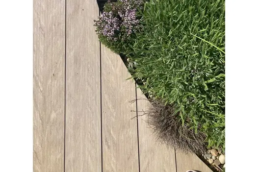 Close view down onto Cinnamon composite planks cut to curve around planted bed with gravel edge. Built by Inspired Gardens.