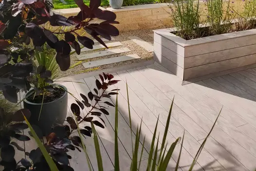 Designed by April House Garden Design www.april-house.co.uk | Built by EWB Services
View through foliage shows Cinnamon DesignBoard Composite Decking used on patio area and clad around built in flowerbeds.