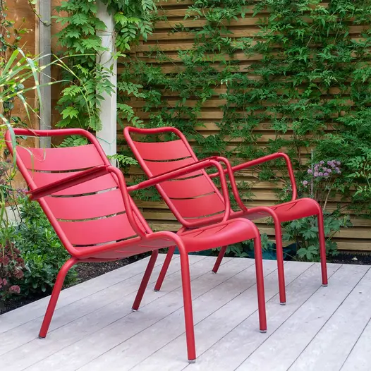 2 red chairs sit in corner of Cinnamon composite decking, slatted fence with climbers in background. Design by A Ryan-Mills.