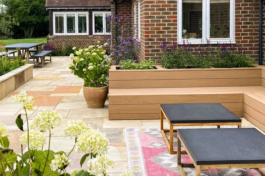 Bench of Cinnamon composite decking backed by inbuilt planters on paved patio wrapped round house. Design by Marlene Lento.