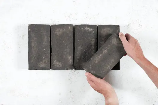 A hand places a paver at angle on top of 4 Durham Clay Paver Bricks, showing texture and shade variations. Available nationwide.