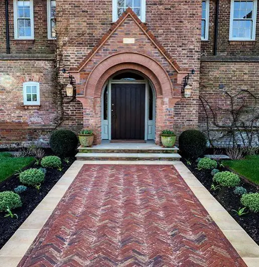 Wide path of Old English clay bricks laid on edge, bordered with paving slabs, leads to front door with gothic-roof porch.
