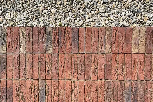 3 courses of red and grey Old English clay pavers laid in stack bond pattern, next to pale gravel. 