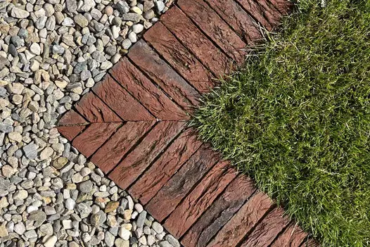 Mitred corner of Old English clay paver bricks laid in soldier course creates edge between mown grass and gravel.