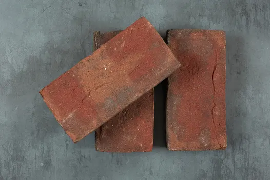 2 Old English clay pavers laid flat with 3rd sitting at angle on top of left one. Showing aged appearance and red tones.